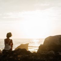 mujer en bañador blanco sentada en una roca mirando al mar