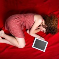 donna distesa sul lenzuolo rosso del letto accanto alla cornice vuota