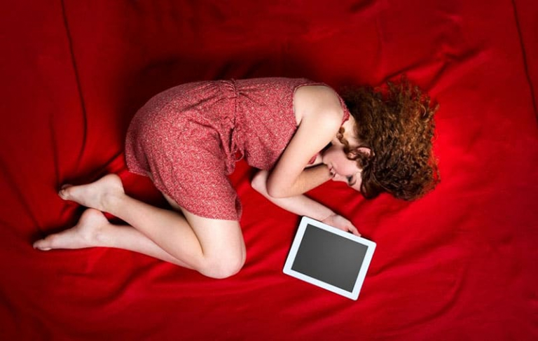 donna distesa sul lenzuolo rosso del letto accanto alla cornice vuota