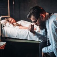mujer tumbada en la cama del hospital cerca de un hombre barbudo que siente pena sentado