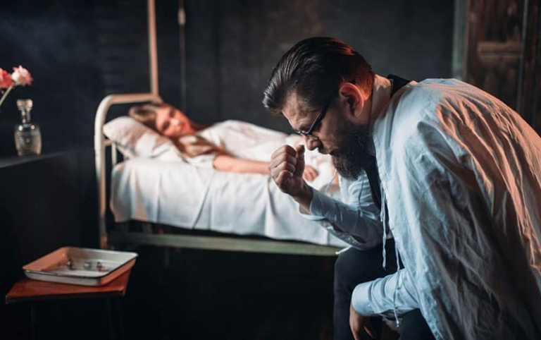 woman lying on the hospital bed near a bearded man feeling sorrow sitting
