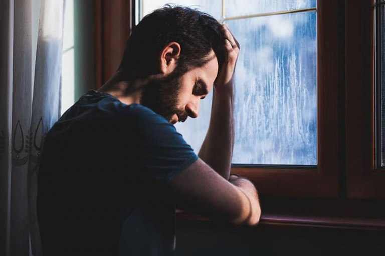 pensive man by the window with hand on his head while raining outside