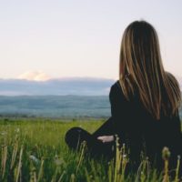 woman in black top sitting on grass looking at mountains