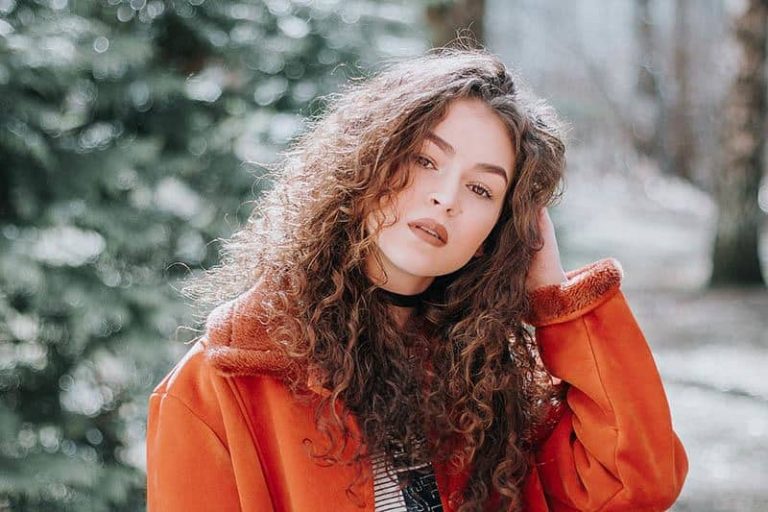 a woman with frizzy hair stands outside and thinks