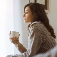 donna pensante seduta e con una tazza di caffè in mano