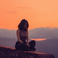 woman sitting on cliff during sunset