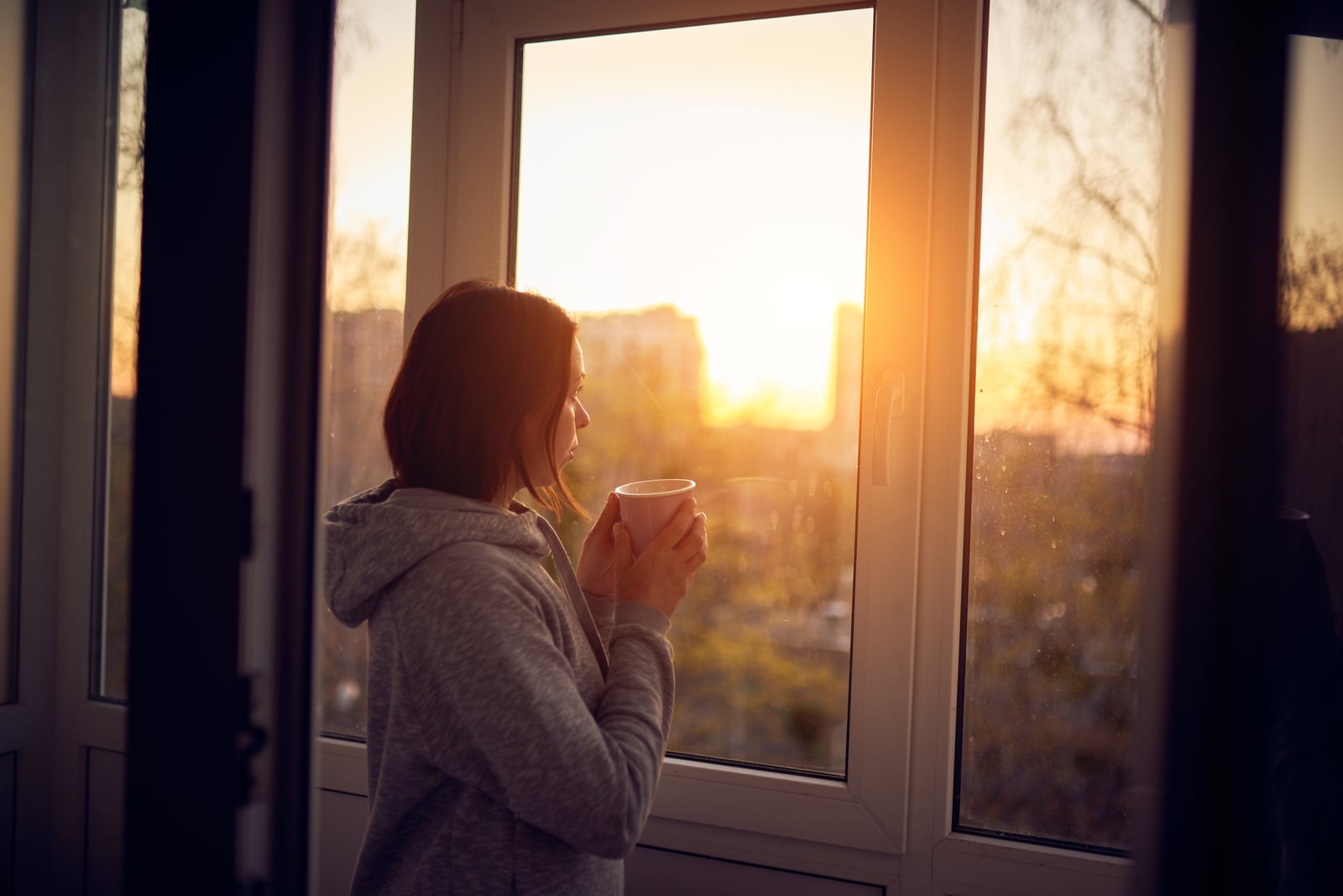 a woman is standing by the window with coffee in her hand