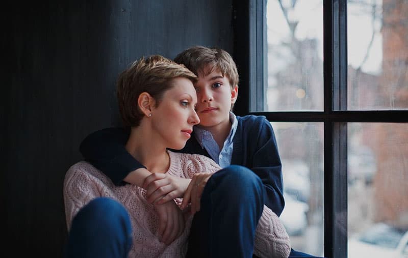 a young boy hugging a sad woman near the windows