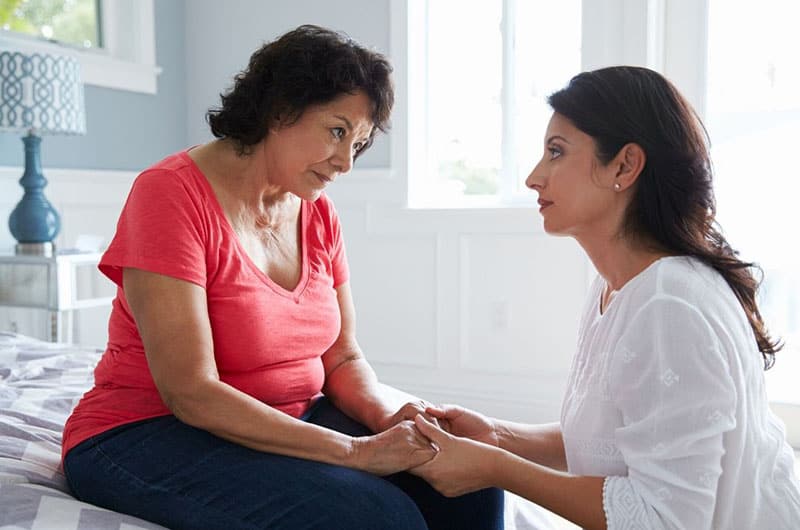 Donna adulta che tiene la mano di una donna anziana mentre si inginocchia davanti a lei