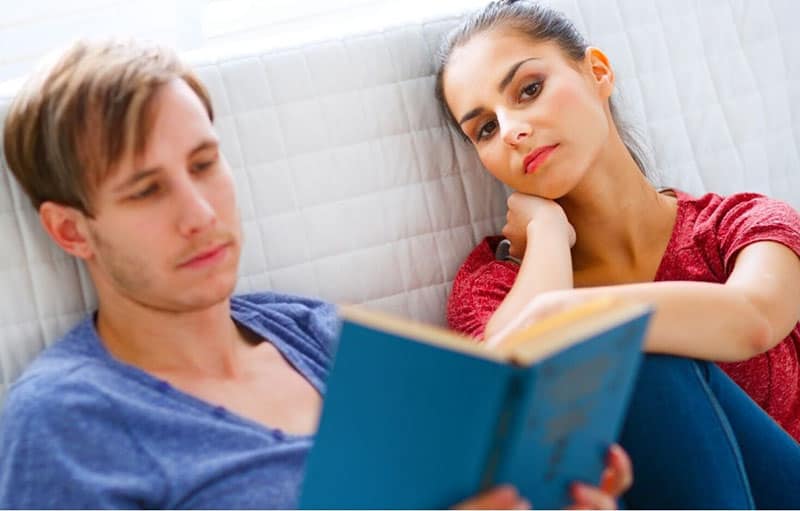 mulher aborrecida sentada ao lado de um homem a ler um livro