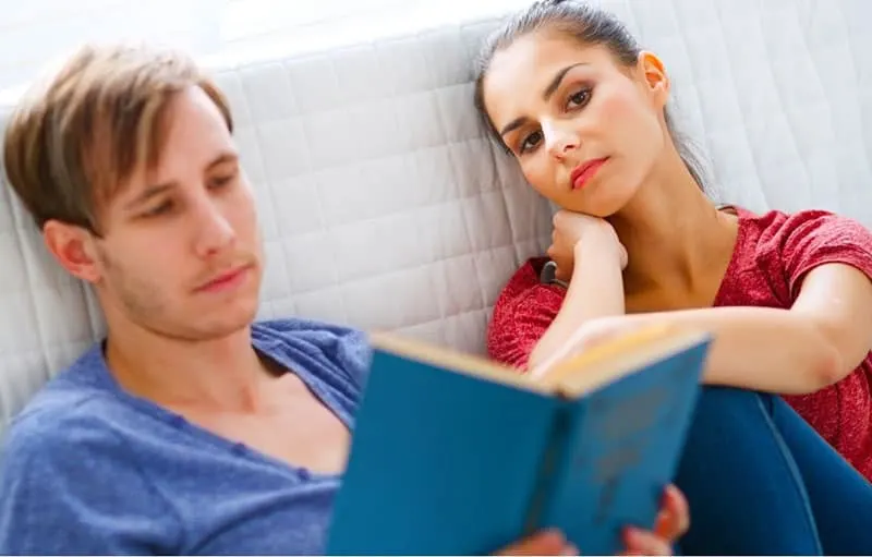 bored woman sitting next to a man reading a book