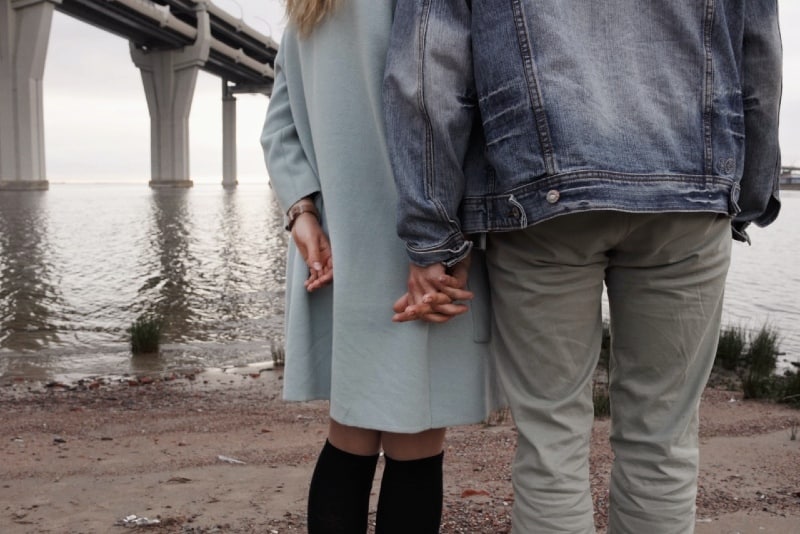 man and woman holding hands while looking at water