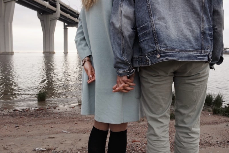 uomo e donna che si tengono per mano guardando l'acqua