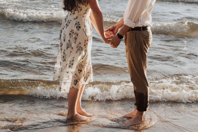 man and woman holding hands while standing on seashore