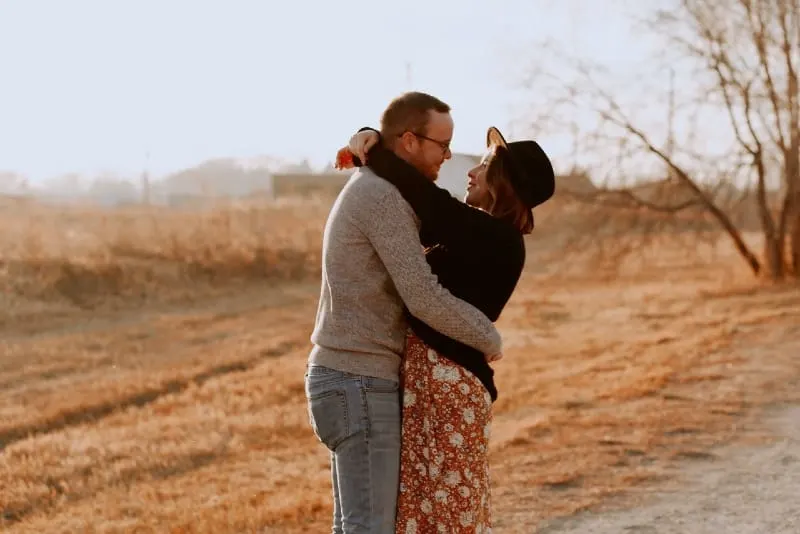 woman with hat and man hugging in field