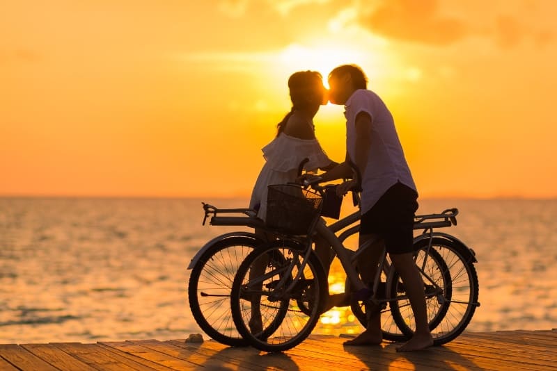 uomo e donna che si baciano tenendo la bicicletta vicino all'acqua