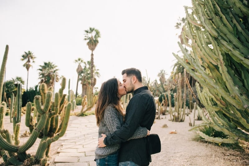 man and woman kissing while standing near cactus