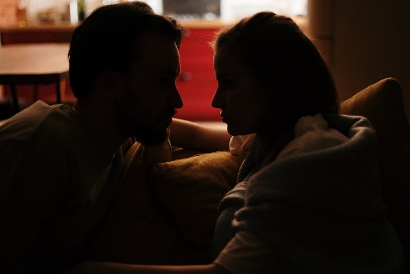 man and woman making eye contact while sitting on sofa