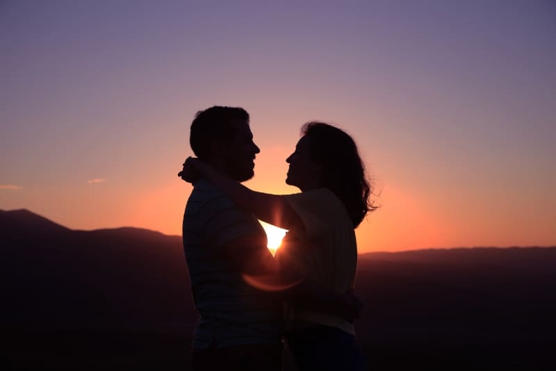 uomo e donna che si guardano negli occhi e si abbracciano durante il tramonto