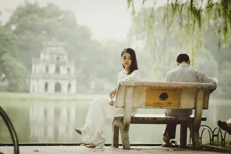woman in white dress and man sitting on bench near water