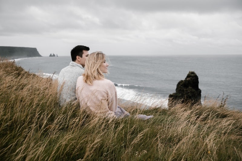 uomo e donna seduti sull'erba che guardano l'oceano