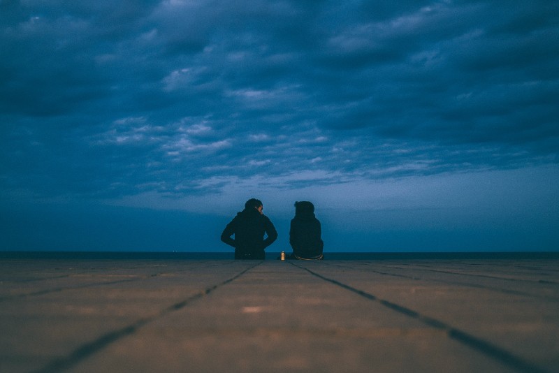 man and woman sitting on ground near sea