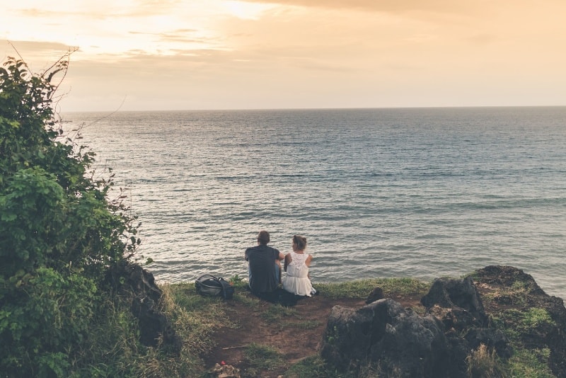 man and woman sitting on ground looking at sea