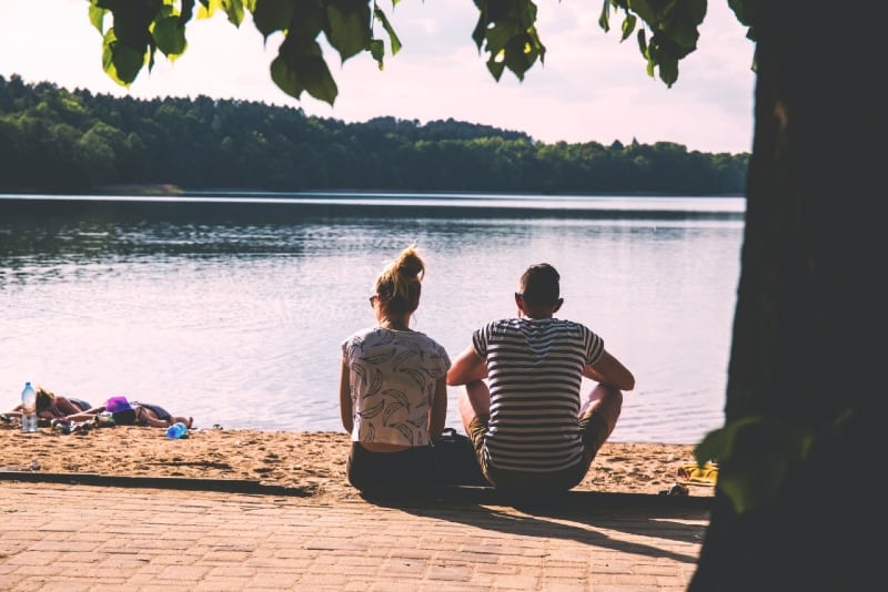 man and woman sitting on pavement near water