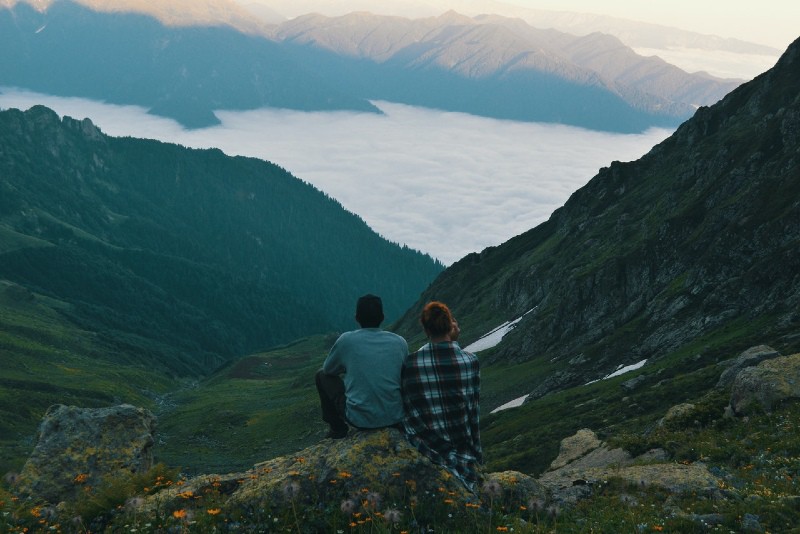 hombre y mujer sentados en una roca mirando la montaña