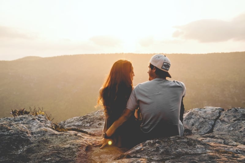 man with cap and woman sitting on rock near mountain