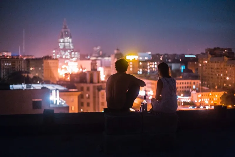 man and woman sitting on rooftop looking at buildings