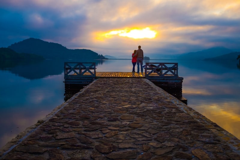 hombre y mujer de pie en el muelle durante la puesta de sol