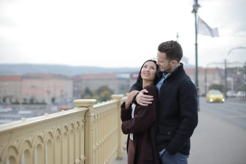 man hugging woman while standing on the bridge