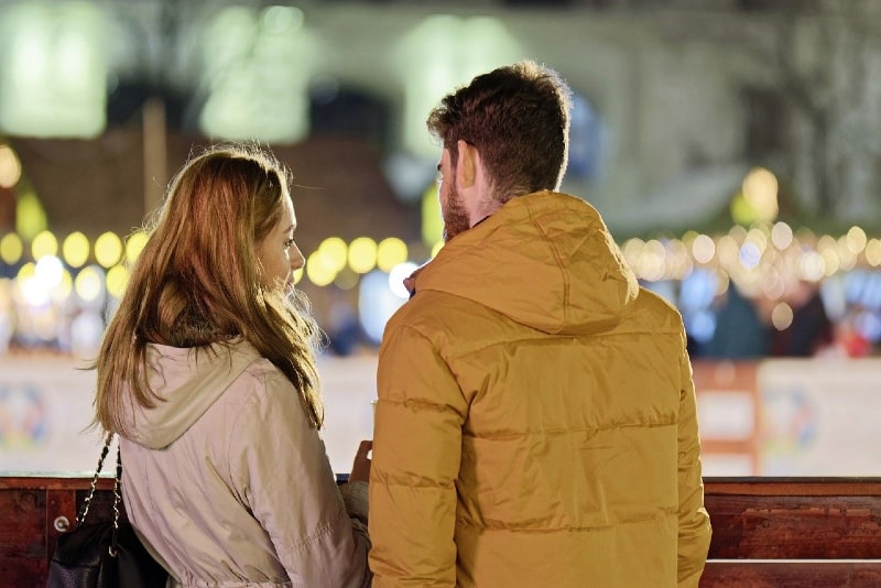 hombre con chaqueta amarilla y mujer hablando al aire libre