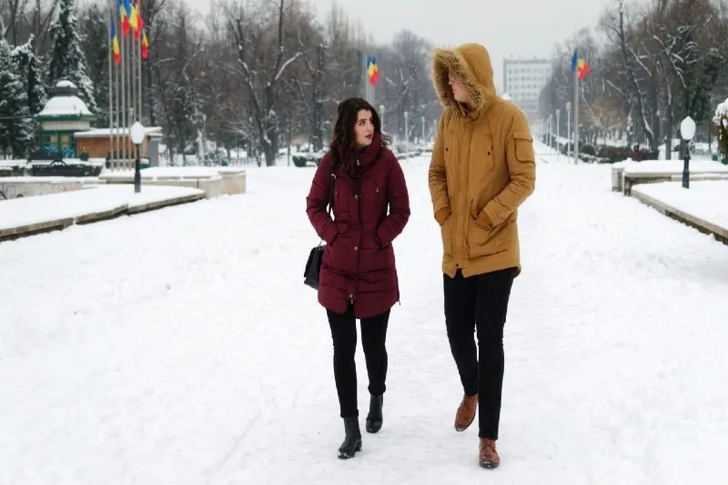 man in yellow jacket and woman walking in snow