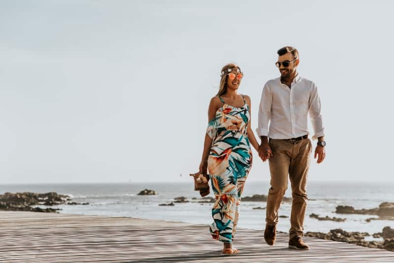 man and woman holding hands and walking near sea