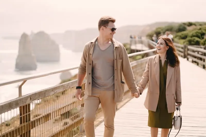 smiling man and woman holding hands while walking on bridge