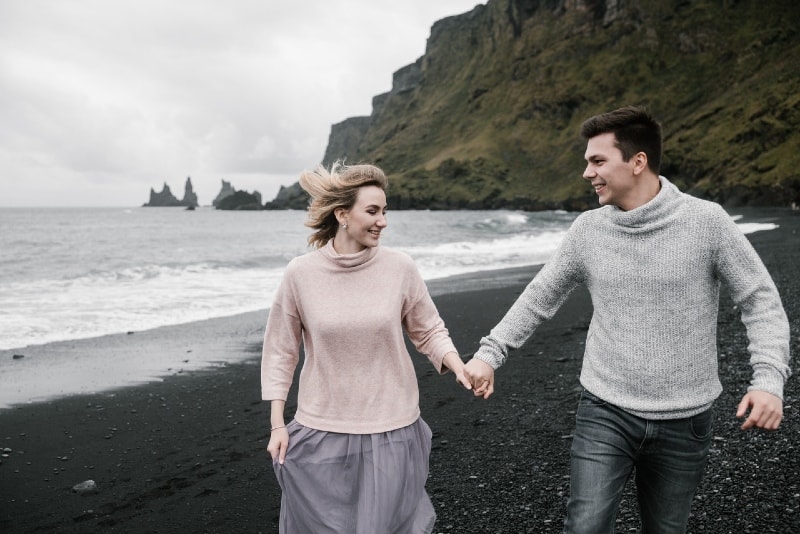 hombre y mujer sonrientes cogidos de la mano caminando por la orilla del mar