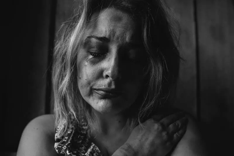 crying abused woman embracing herself in the dark