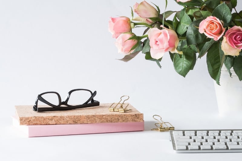 occhiali da vista su un libro vicino a un vaso con rose