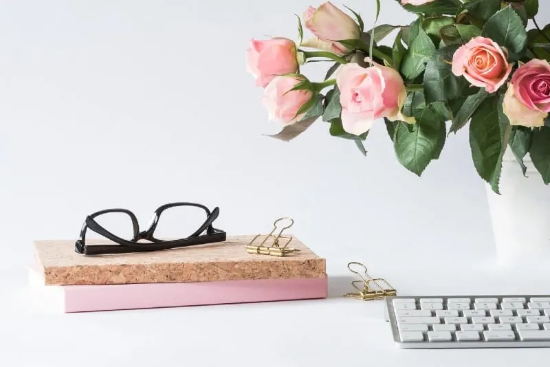 eyeglasses on book near vase with roses