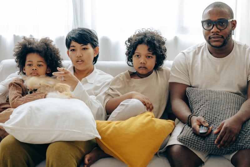 mulher, marido e dois filhos a ver televisão com o cão