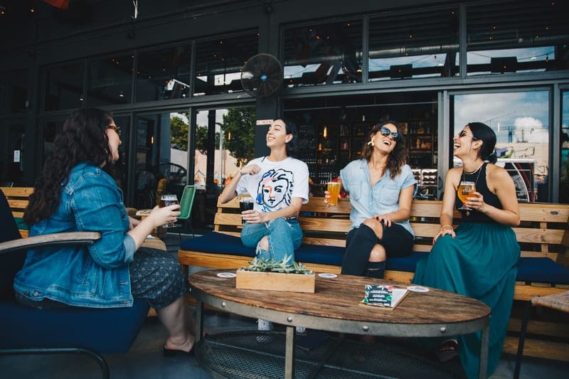 cuatro mujeres charlando y riendo al aire libre con bebidas a mano