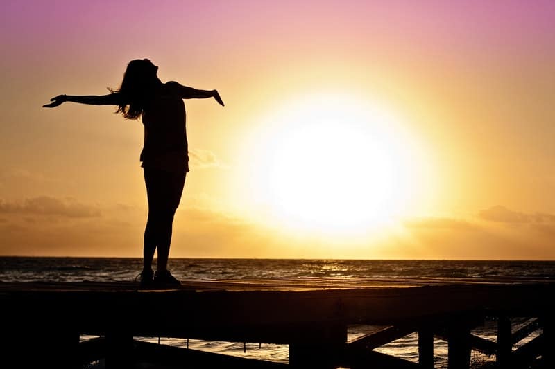 donna libera che allarga le braccia vicino alla spiaggia in piedi di una piattaforma di legno in silhouette