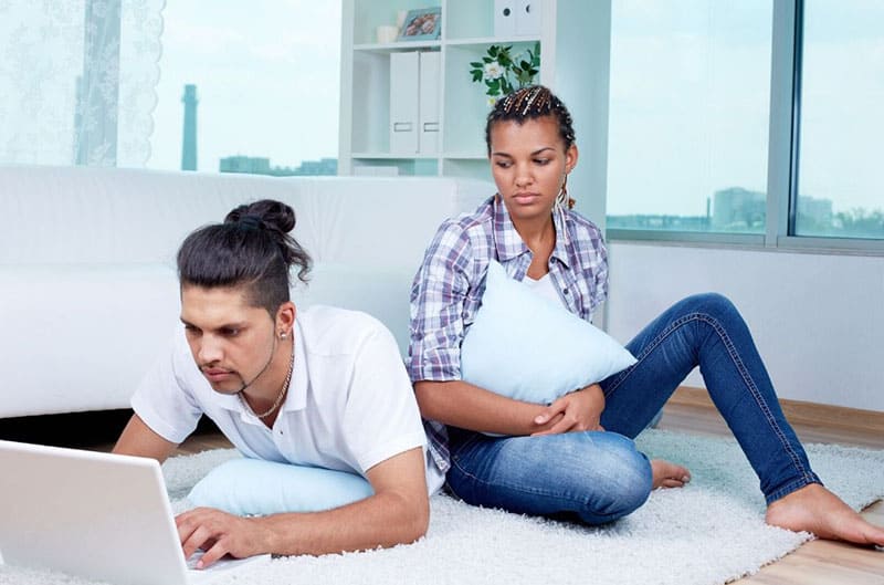 jealous woman while man on laptop networking placed on a white rug