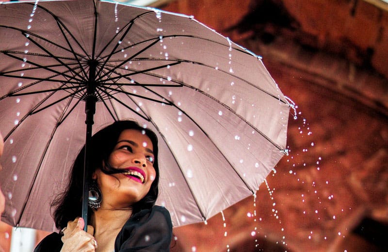 vista dall'angolo basso di una donna che si guarda indietro e sorride tenendo in mano un ombrello per proteggersi dalla pioggia