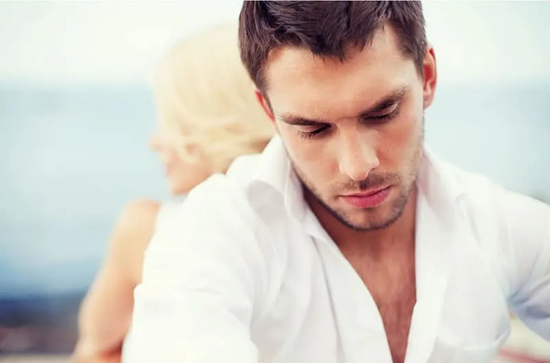 man and woman back to back looking sad sitting wearing white top
