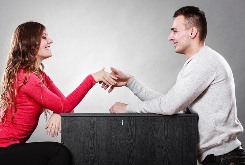 man and woman shake hands while sitting face to face and hands on the table 