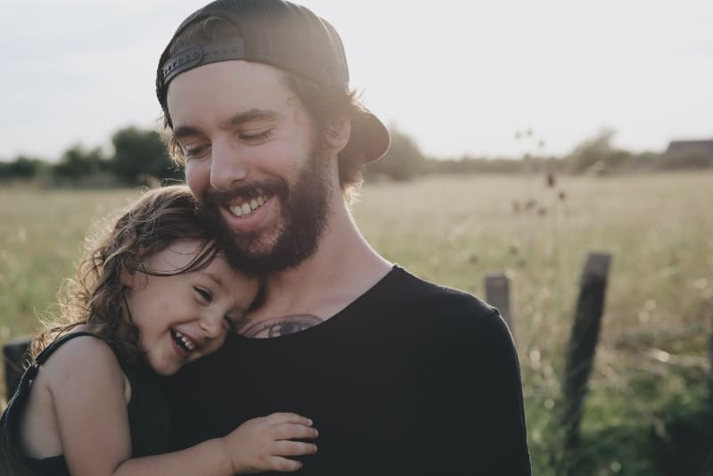 uomo sorridente con maglietta nera che porta la figlia all'aperto