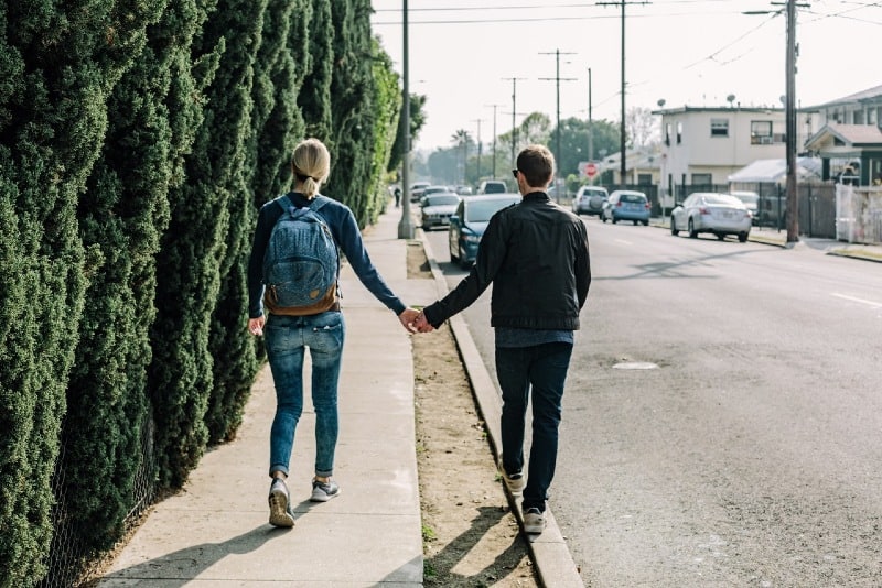 man holding woman's hand while walking on sidewalk